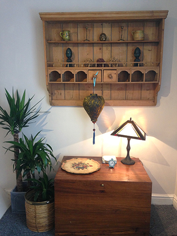 Wooden chest under a decorative wooden wall unit with ornaments, lamp and plants