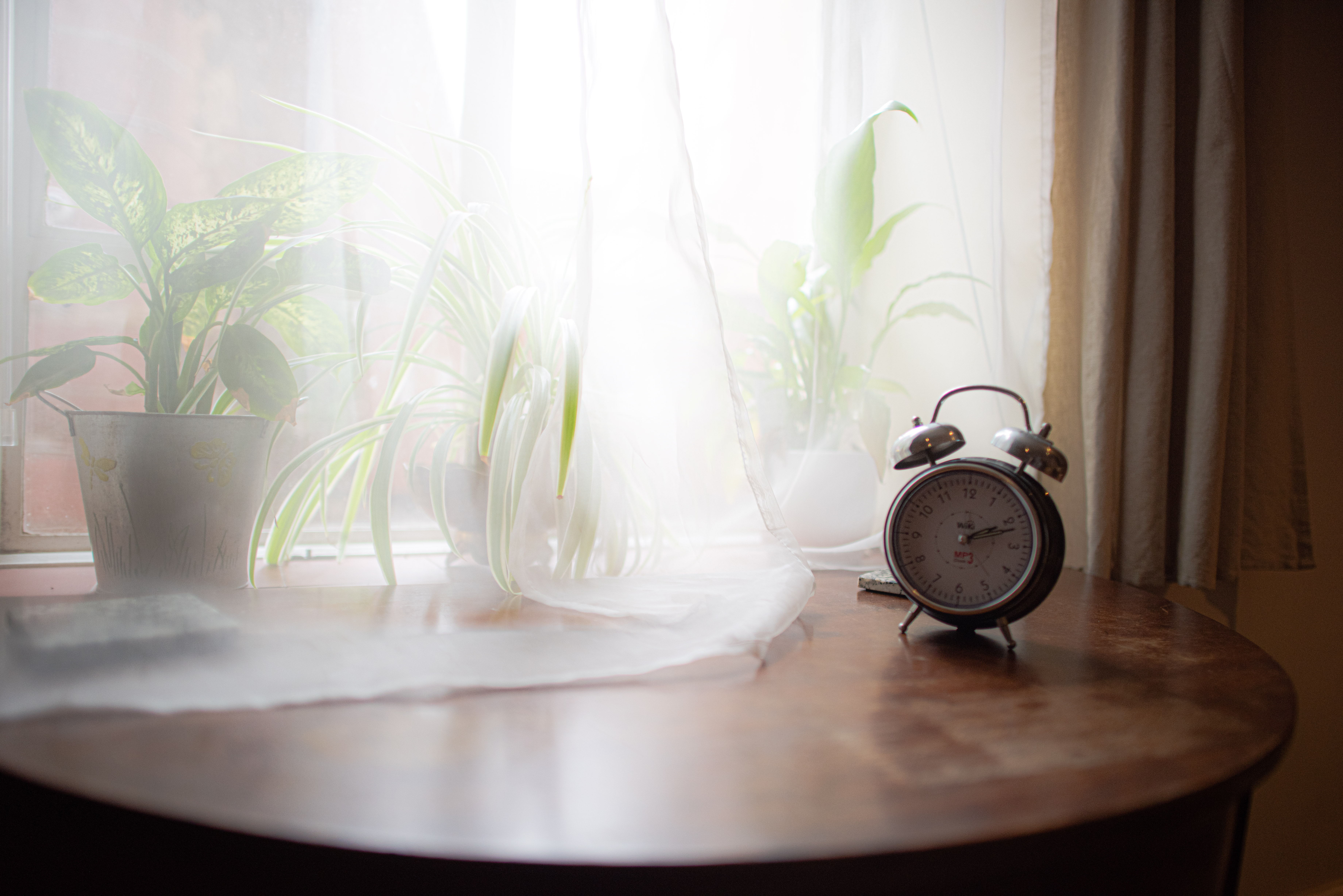 A clock on a wooden table by the window