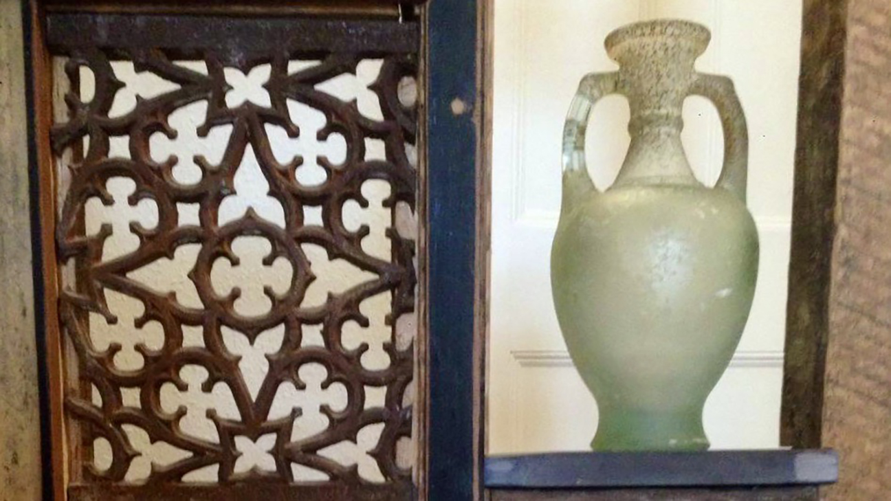 White vase next to a decorative metal grate