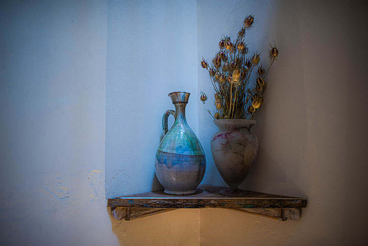 A blue jug and some dried flowers perched on a shorner shelf